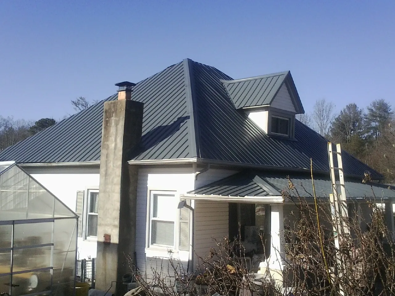 Dark blue standing seam metal roof on a white farmhouse with dormer — Slate & Tile Roof Repair by Roofing Brothers in George West