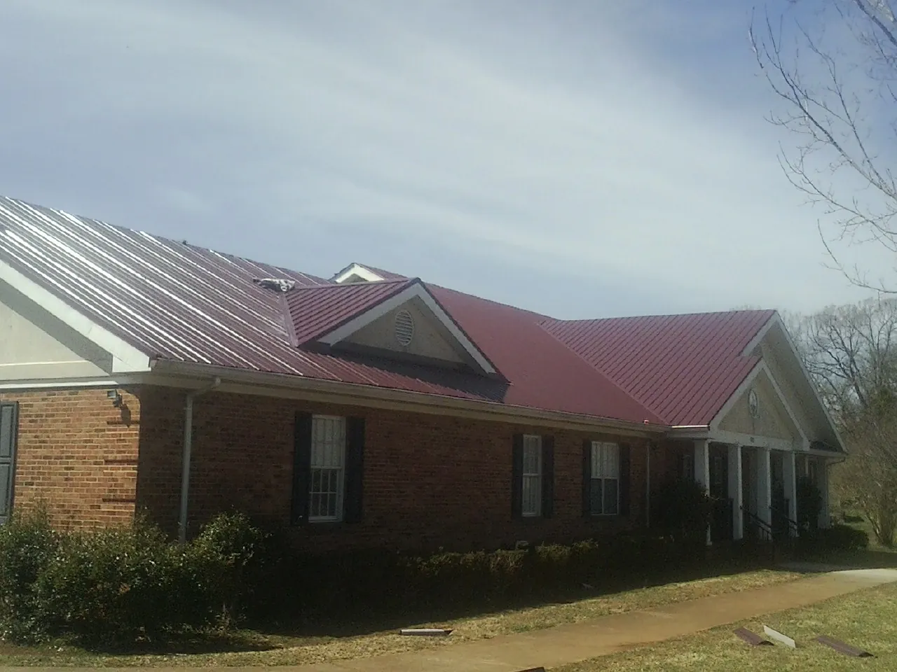 Red metal roof with gabled entries on a long brick building, from a Hail Damage Roof Repair job in George West