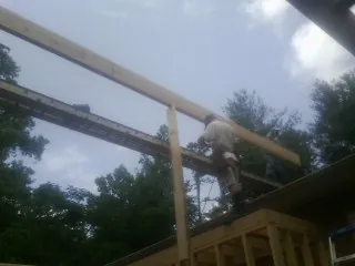 Carpenter setting a ridge beam over a new addition frame in George West