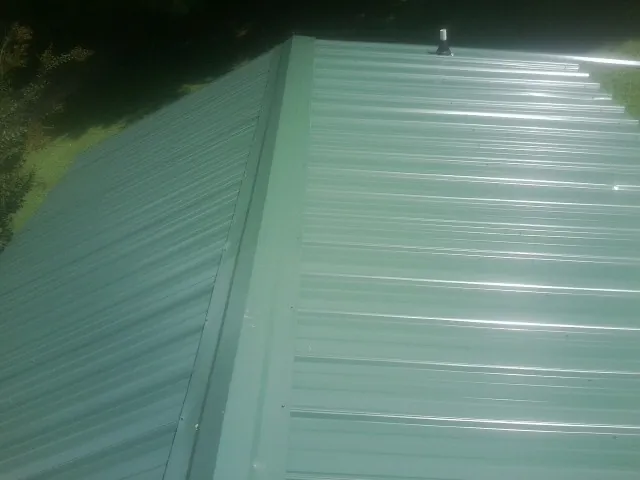 New green metal panels meeting at the ridge of a roof — Flat Roof Repair work by our crew in George West