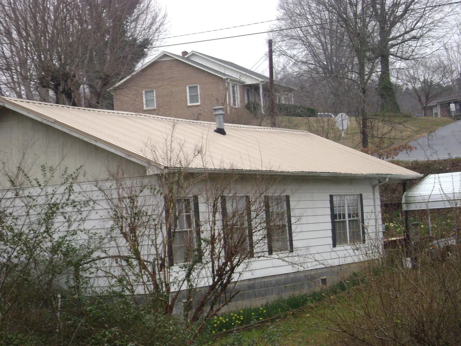 Tan metal roof on a white sided house set into a hillside — Commercial Roofing by Roofing Brothers in George West