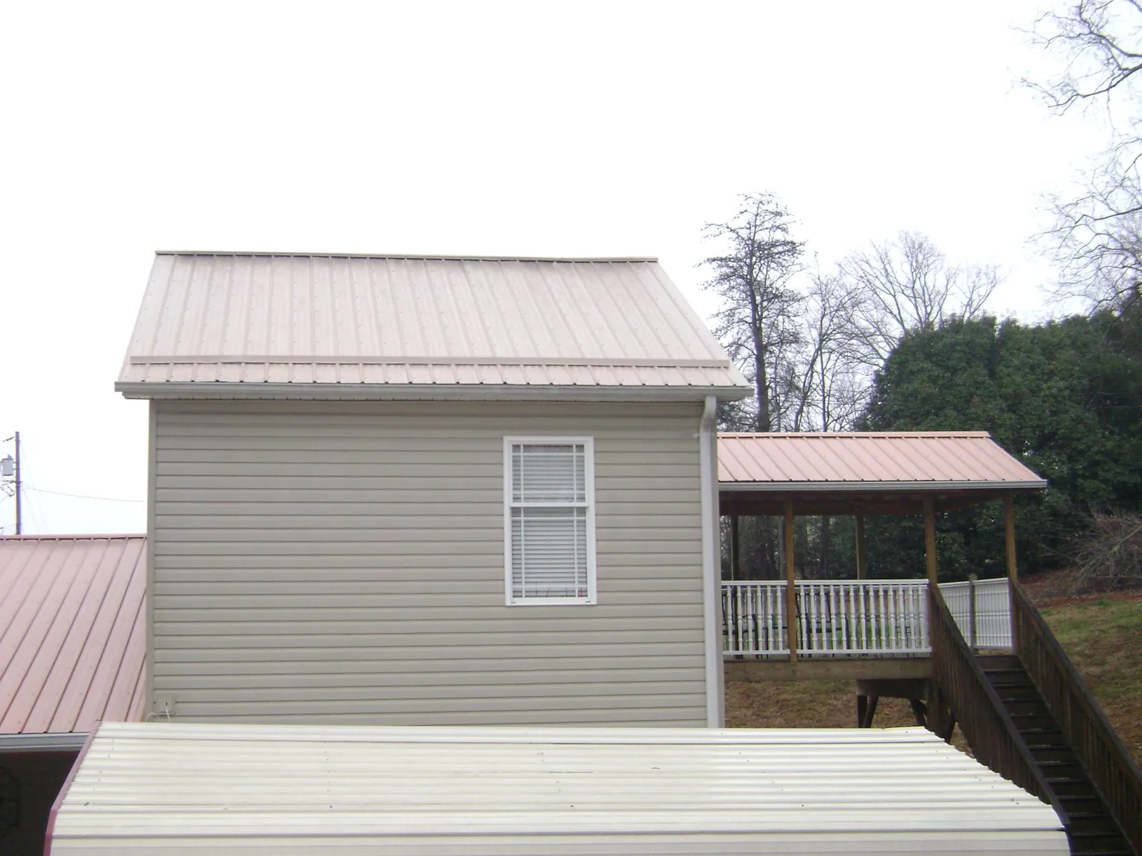 Tan metal roofs on a two story addition and attached porch, from a Roof Replacement job in George West